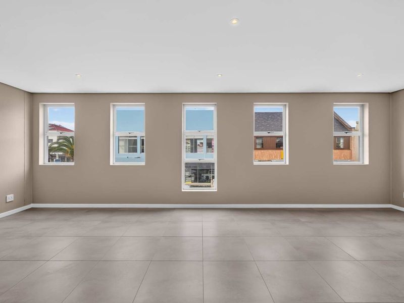 A spacious, empty living area featuring neutral-toned walls, large vertical windows providing natural light, and modern tiled flooring throughout.