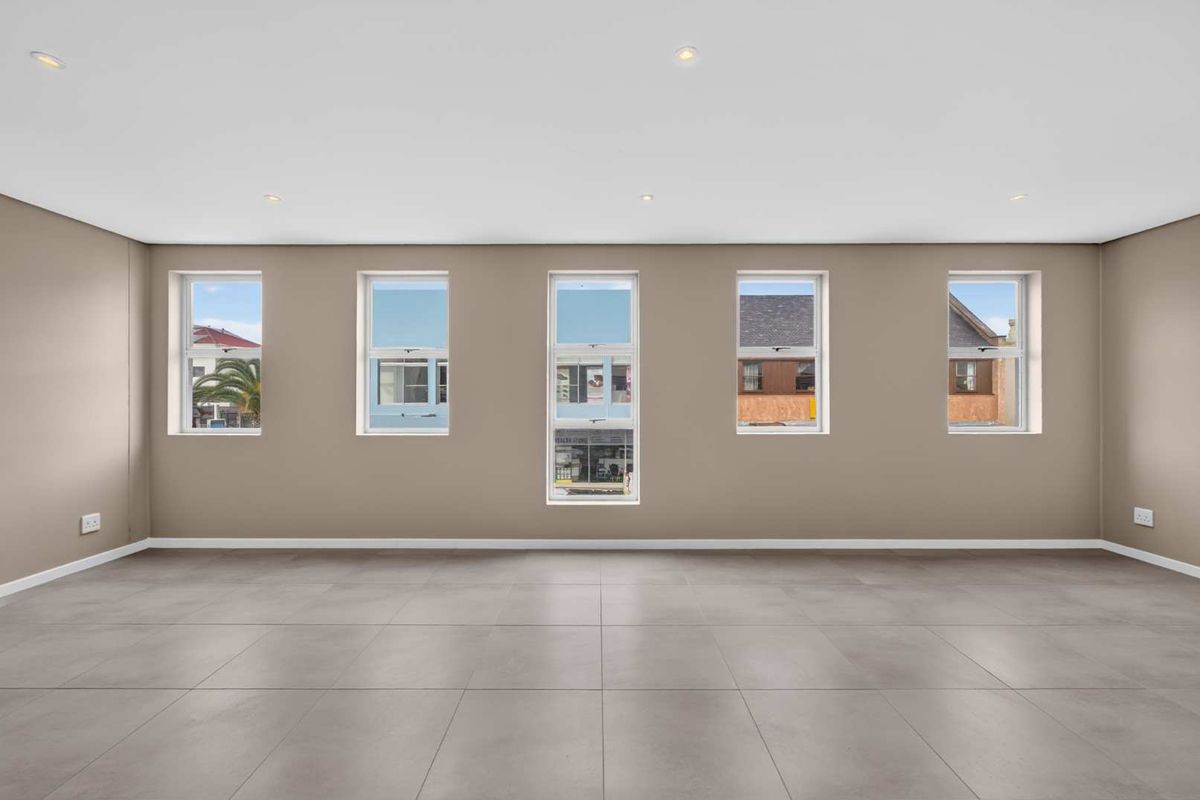 A spacious, empty living area featuring neutral-toned walls, large vertical windows providing natural light, and modern tiled flooring throughout.