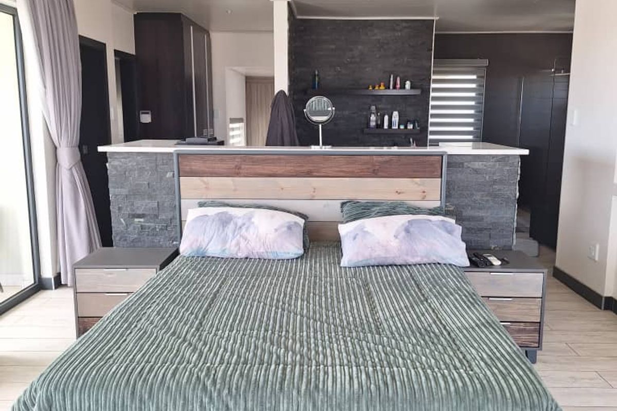 Spacious bedroom featuring a central stone-clad partition wall, integrated headboard, tiled flooring, and built-in cabinetry with direct access to an en-suite area.