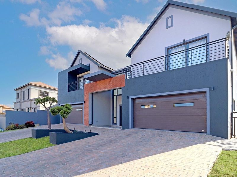 Modern double-story residential facade featuring a paved driveway, double garage, and an upper-level balcony with metal railings.
