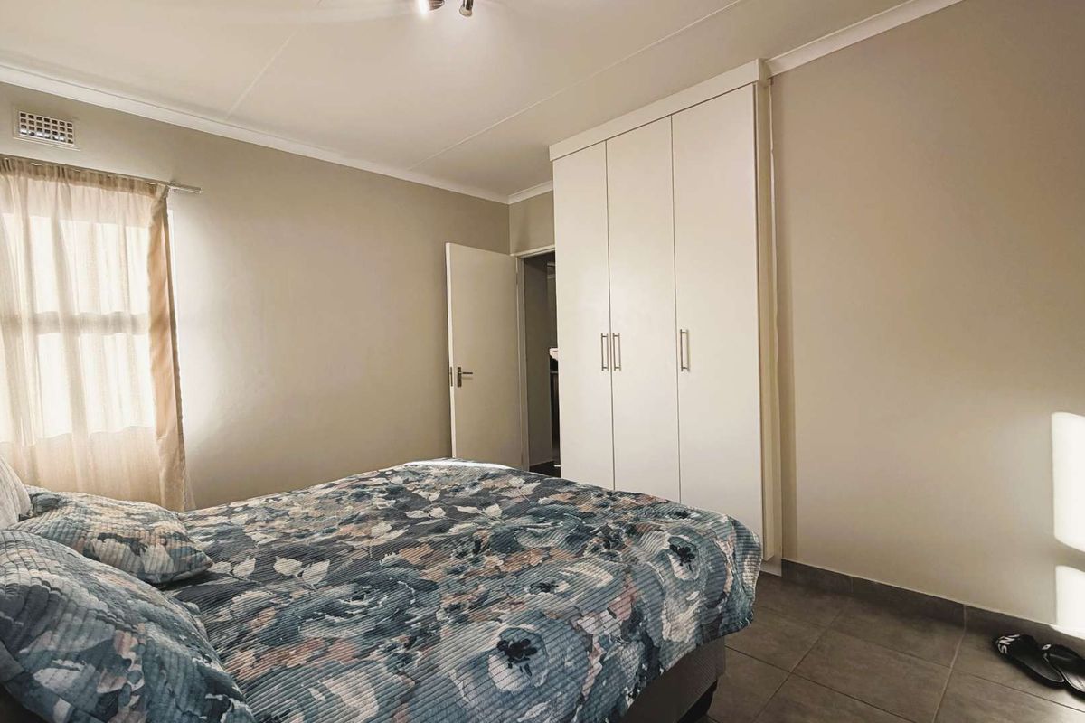 A bedroom featuring built-in white wardrobes, tiled flooring, and a window with neutral curtains.