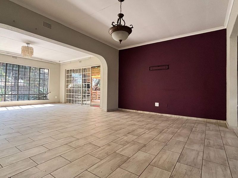 Spacious, light-filled living area featuring neutral tiled flooring, an arched transition, and large steel-framed windows leading to an outdoor patio space.