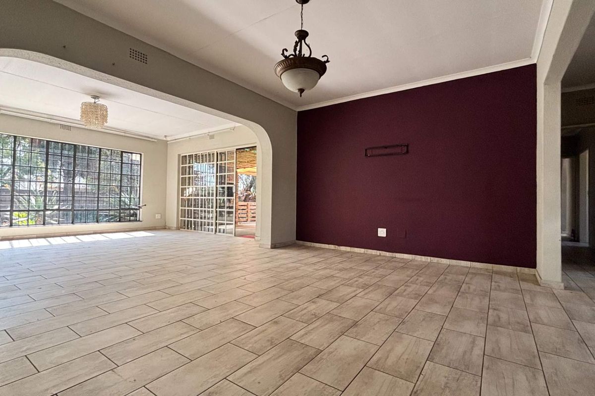 Spacious, light-filled living area featuring neutral tiled flooring, an arched transition, and large steel-framed windows leading to an outdoor patio space.