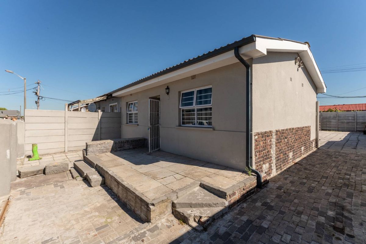 Rear exterior view of the house featuring a paved patio area, concrete steps, and perimeter boundary walling.