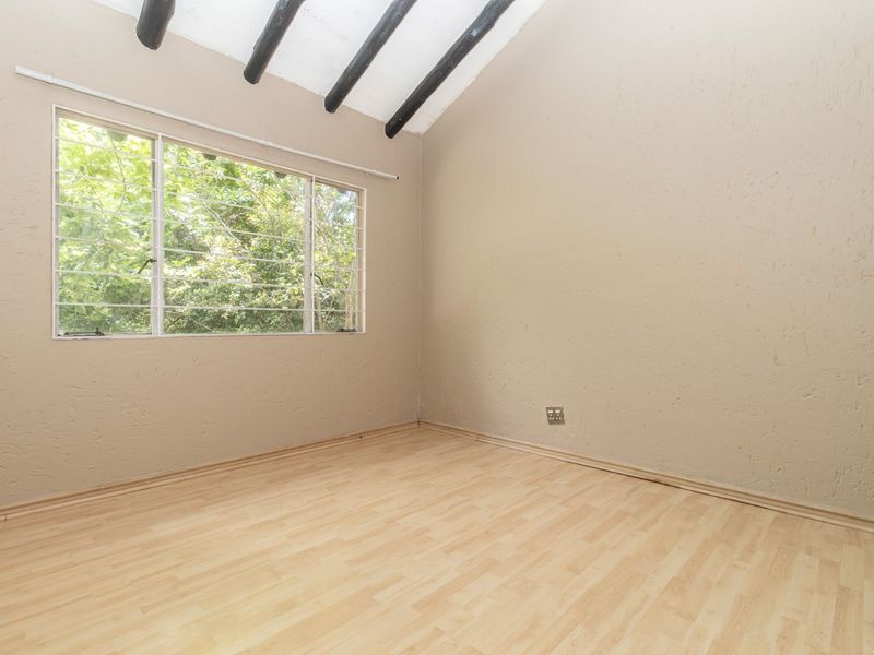 An empty bedroom featuring laminate flooring, textured walls, and exposed timber ceiling beams with a window overlooking greenery.