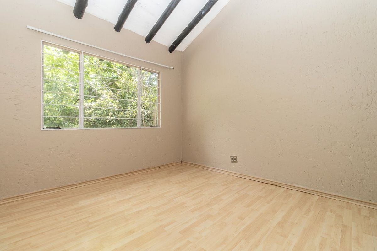 An empty bedroom featuring laminate flooring, textured walls, and exposed timber ceiling beams with a window overlooking greenery.