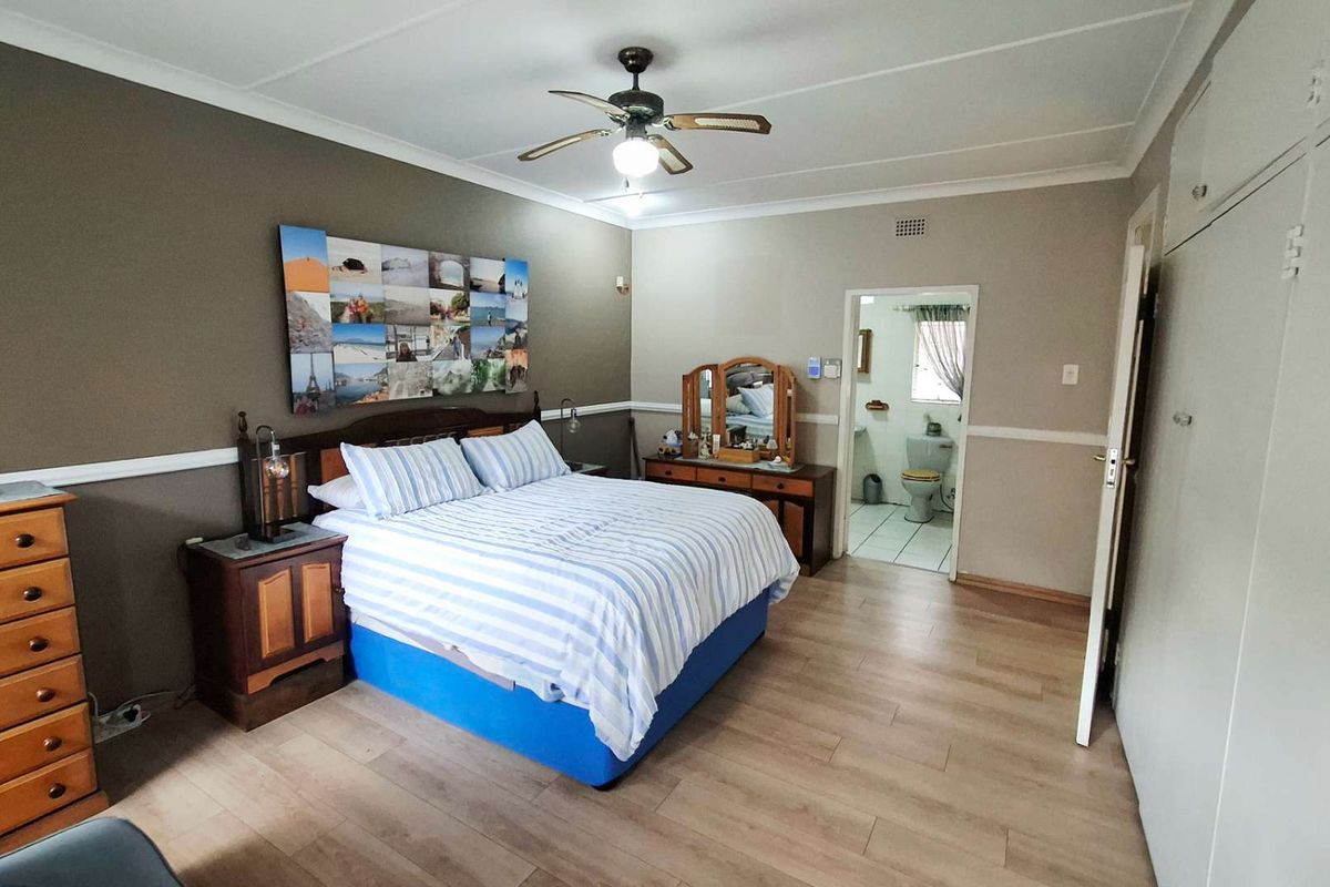 Spacious bedroom featuring laminate flooring, built-in cupboards, and an en-suite bathroom access, offering a functional layout with neutral wall tones.
