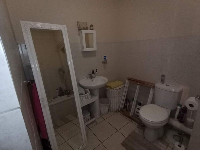 A functional bathroom featuring a pedestal basin, standard toilet, and neutral wall and floor tiling.