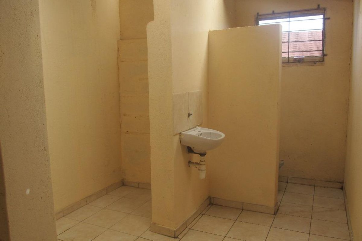 A basic, functional bathroom space featuring tiled flooring, a wall-mounted basin, and a privacy partition wall.