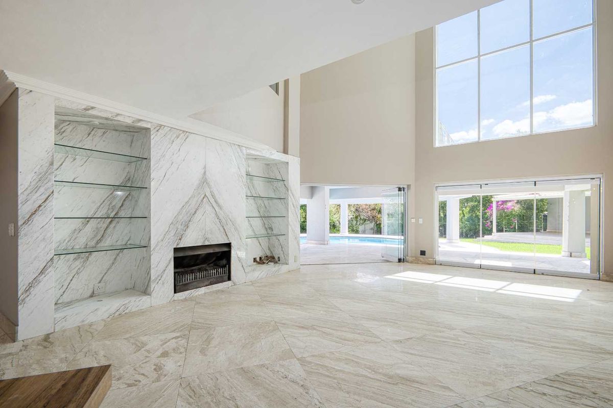 Spacious living area featuring high ceilings, large windows, marble-clad fireplace with built-in shelving, and seamless access to the outdoor patio and pool area.