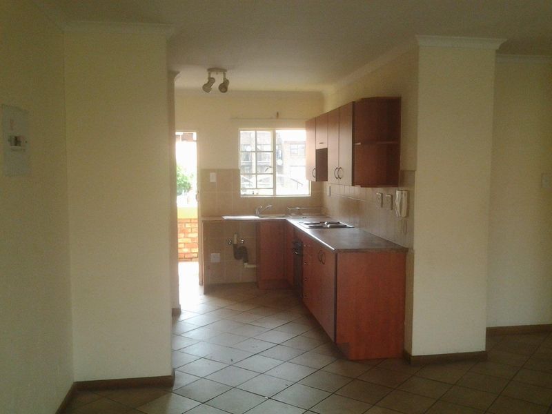 A compact kitchen featuring wooden cabinetry, tiled backsplash, and ceramic flooring, with an adjacent doorway leading to an outdoor area.