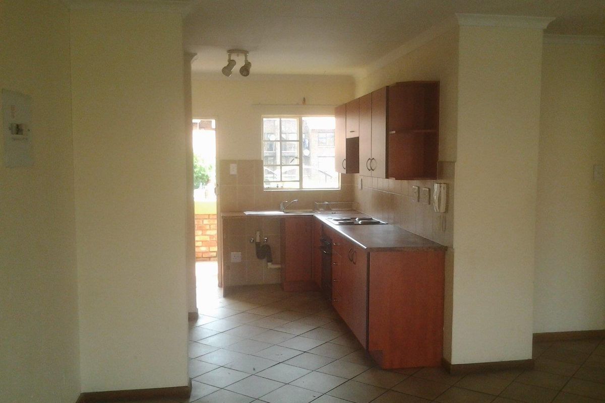 A compact kitchen featuring wooden cabinetry, tiled backsplash, and ceramic flooring, with an adjacent doorway leading to an outdoor area.