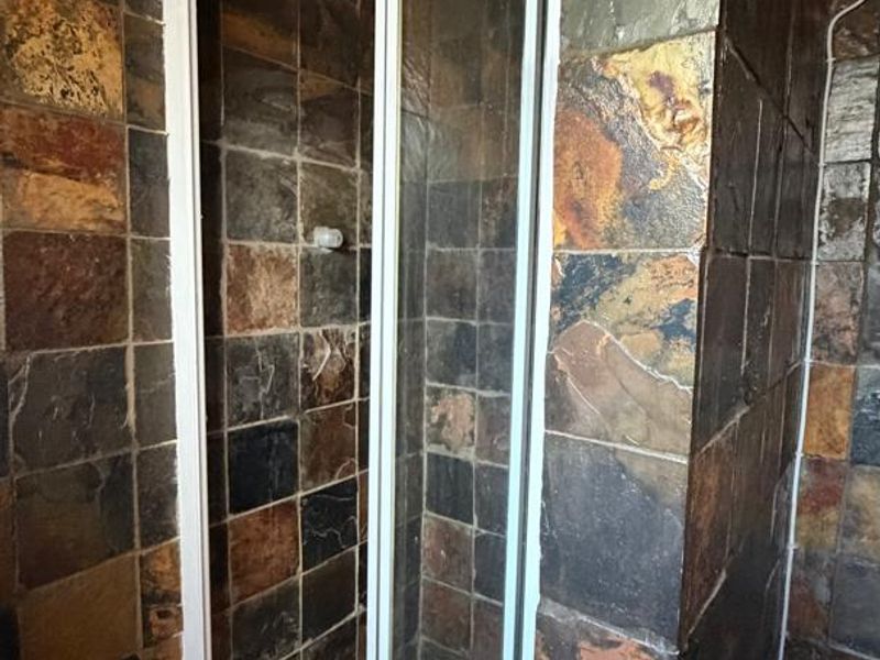 A bathroom featuring a shower enclosure with rustic slate wall tiles and a traditional thatched roof ceiling.