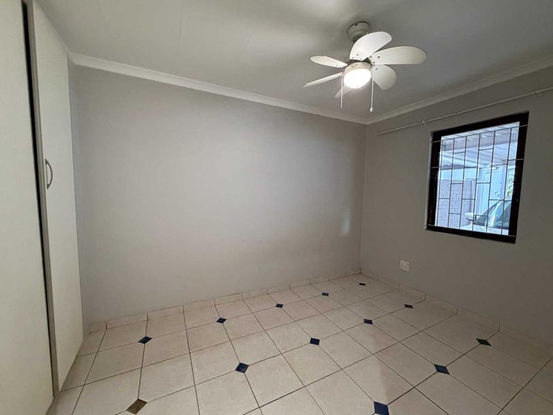 An empty bedroom featuring tiled flooring, a built-in wardrobe, and a ceiling fan, with security bars installed on the window.