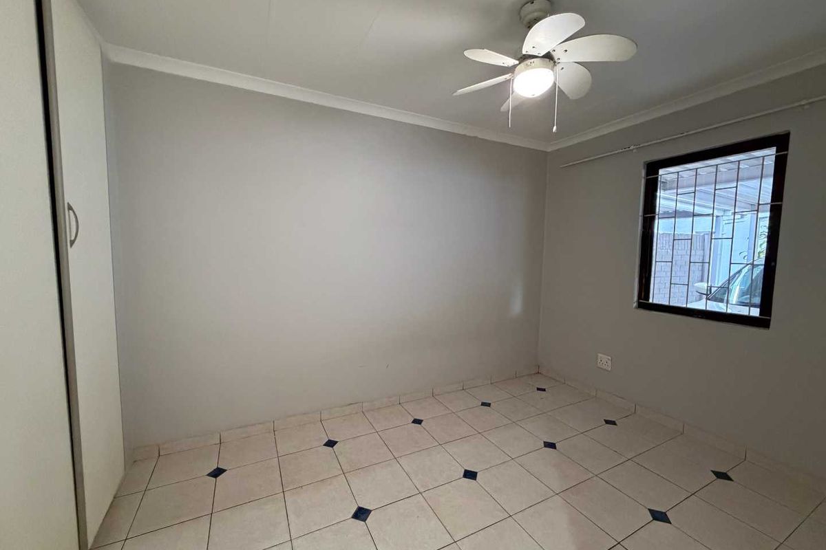 An empty bedroom featuring tiled flooring, a built-in wardrobe, and a ceiling fan, with security bars installed on the window.