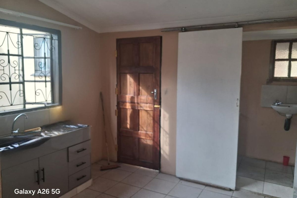 A functional kitchen area featuring built-in cabinetry, a stainless steel sink, tiled flooring, and an adjacent utility space with a wall-mounted basin.