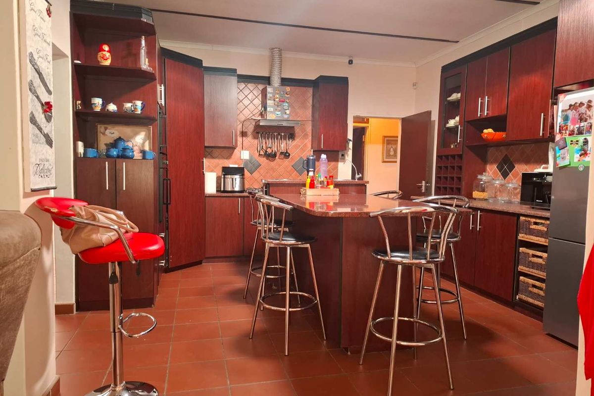 A spacious kitchen featuring dark wood cabinetry, a central island with granite countertops, and tiled flooring, offering a functional layout for cooking and dining.