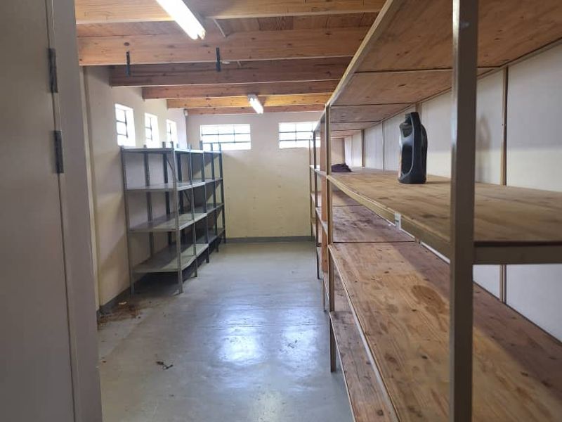 A functional utility or storage space featuring exposed timber ceiling beams, concrete flooring, and high-level windows, providing ample storage potential for industrial use.
