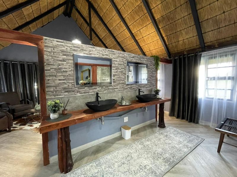 A stylish bathroom featuring a double vanity with vessel sinks, a stone veneer feature wall, and a high exposed thatch roof.