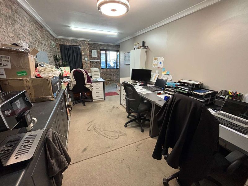 A functional office space featuring exposed brickwork, built-in cabinetry, and security-fitted windows, currently utilized as a workspace.