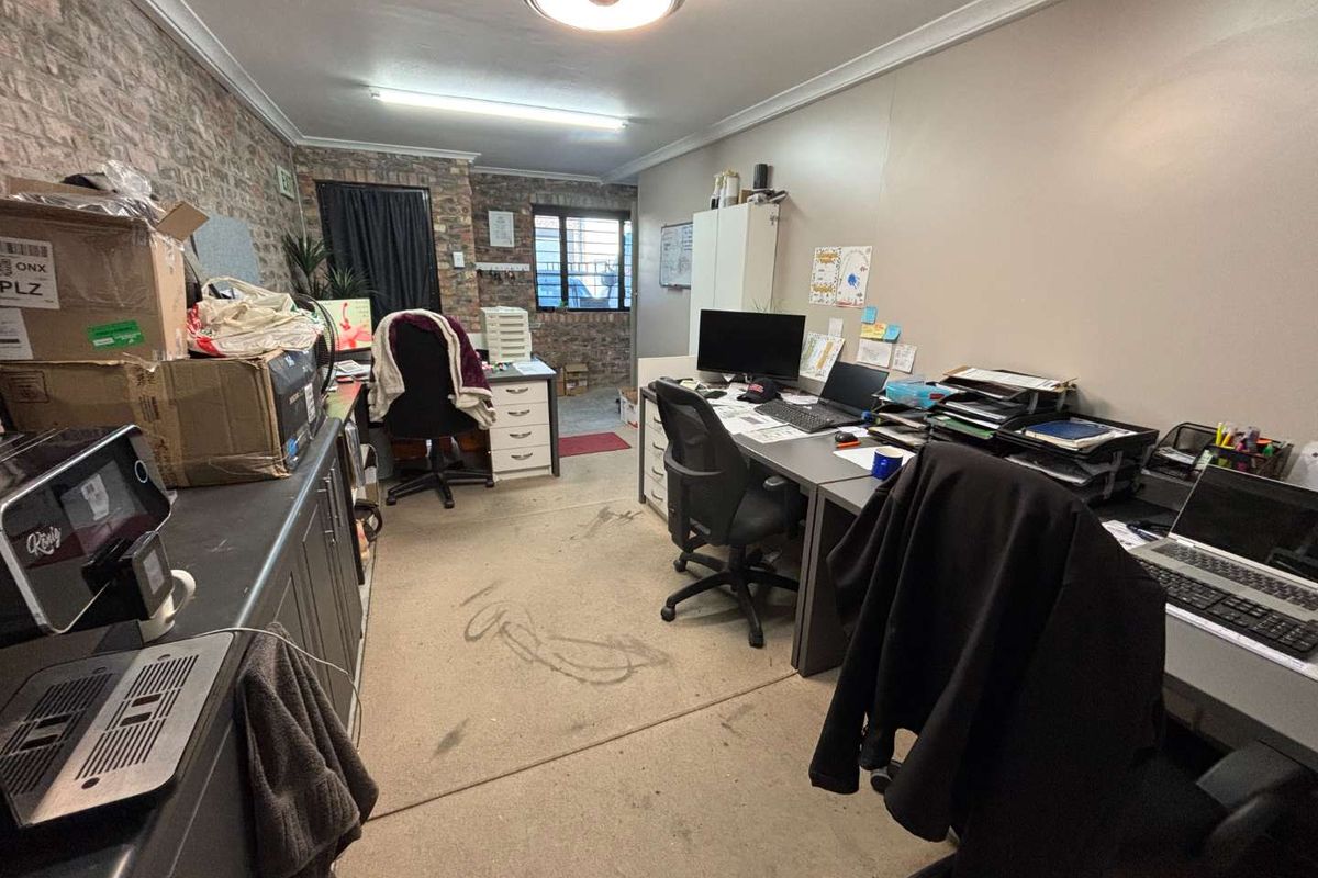A functional office space featuring exposed brickwork, built-in cabinetry, and security-fitted windows, currently utilized as a workspace.