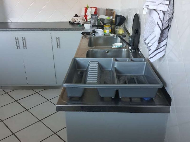 A functional kitchen area featuring a double stainless steel sink, tiled backsplash, laminate countertops, and built-in cabinetry with tiled flooring.