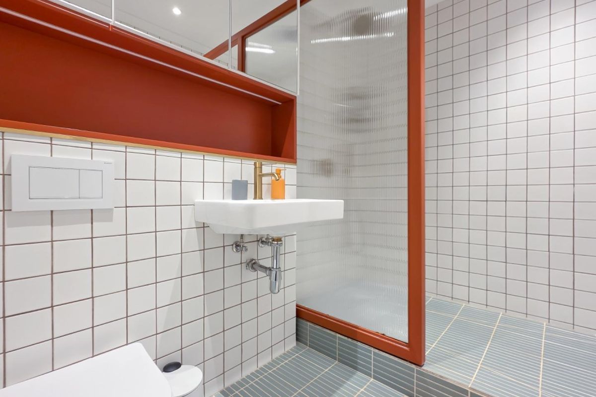Modern bathroom featuring a wall-mounted basin, fluted glass shower screen, wall-hung toilet, and stylish brass fixtures with contemporary white and blue tiling.