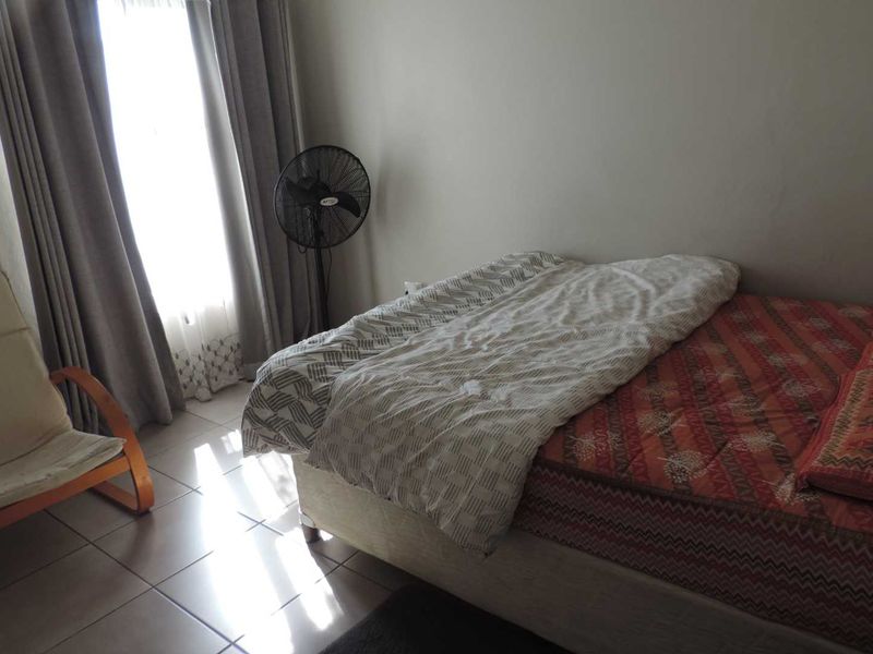 A standard bedroom featuring tiled flooring and natural light through a window with curtain tracks.
