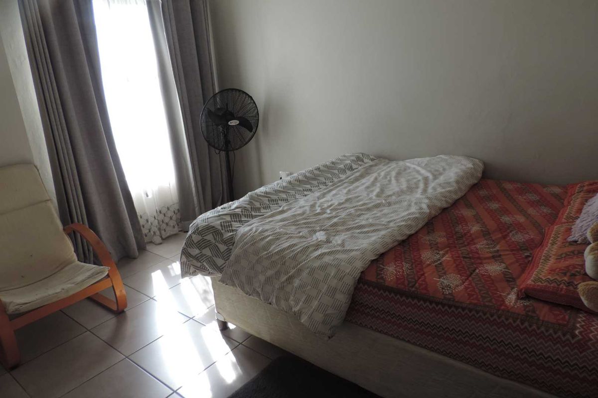A standard bedroom featuring tiled flooring and natural light through a window with curtain tracks.