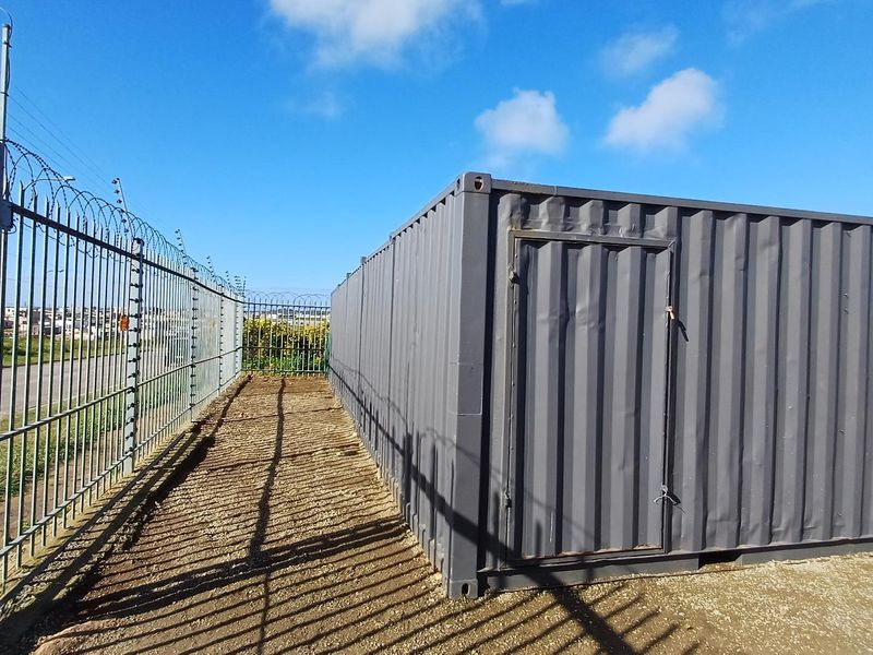 Industrial site featuring a secure steel shipping container unit enclosed by high-security perimeter fencing with electric wiring and razor wire.