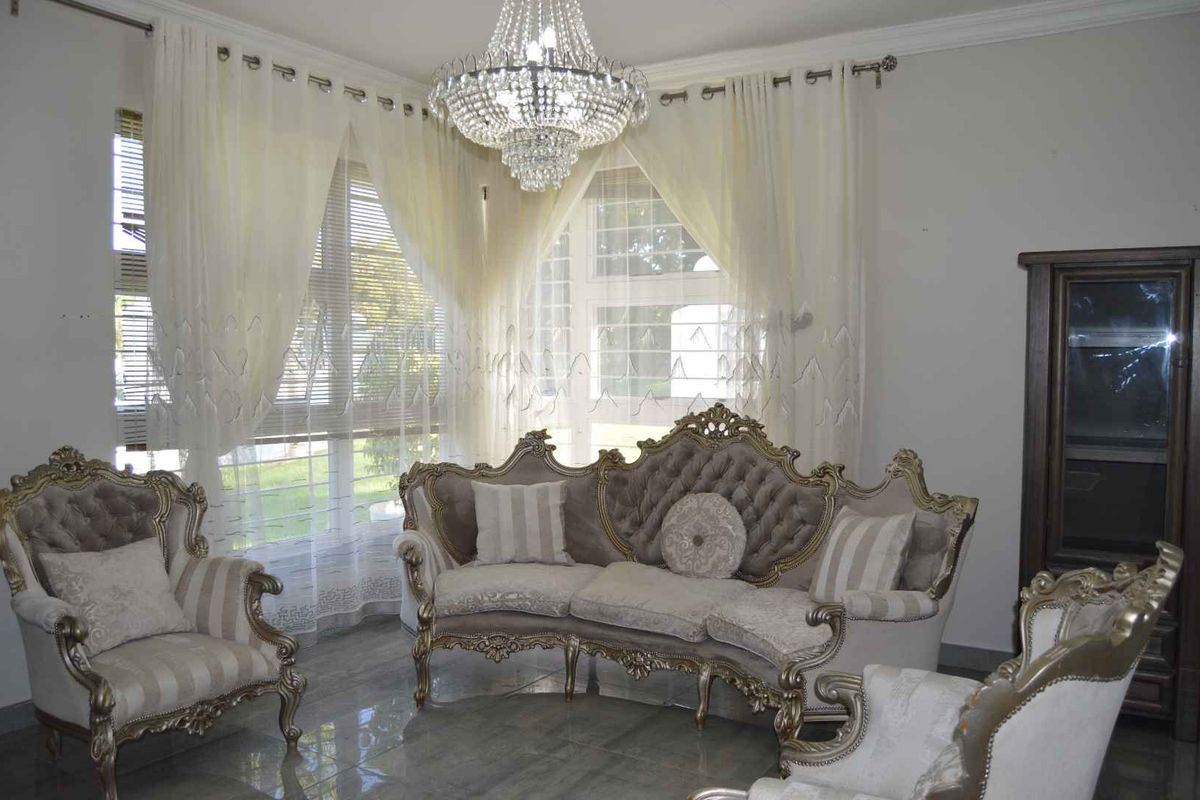 A formal living room featuring polished tiled flooring, large windows with elegant drapery, and a prominent crystal chandelier.