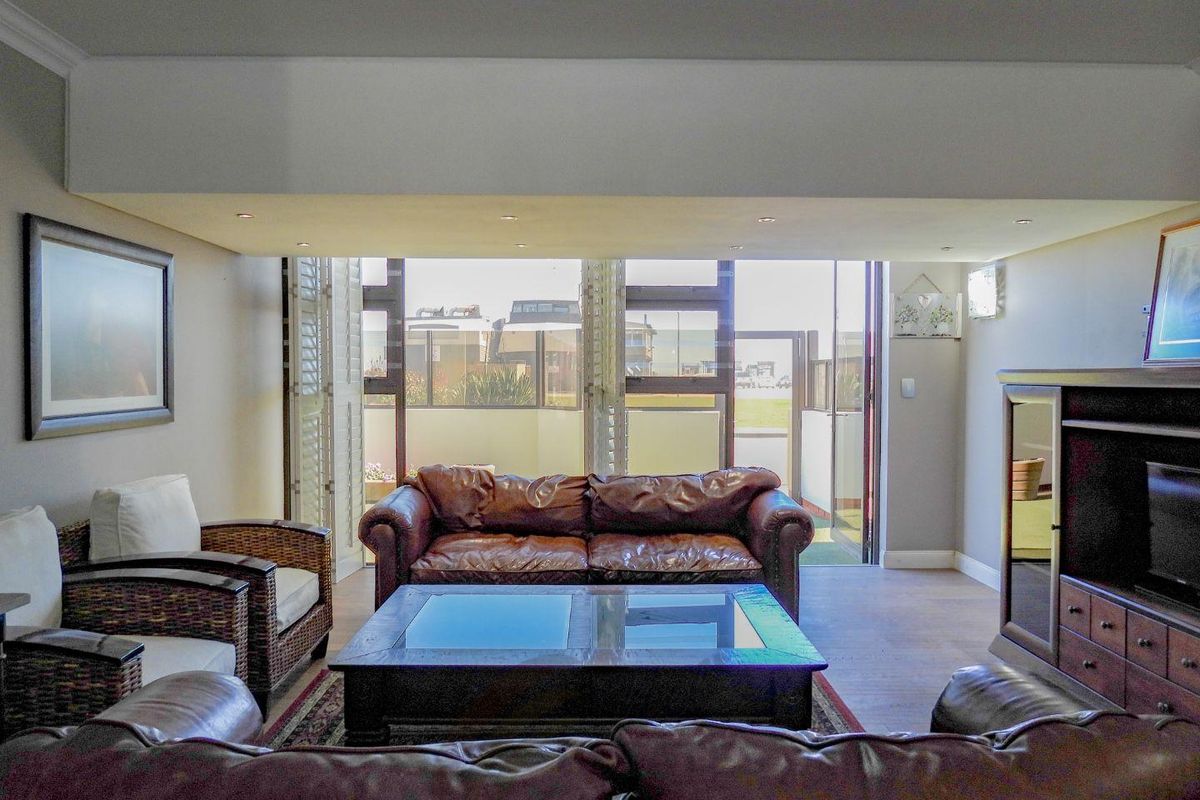 A comfortable living room featuring recessed ceiling lighting and large folding shutters that open onto a private balcony.