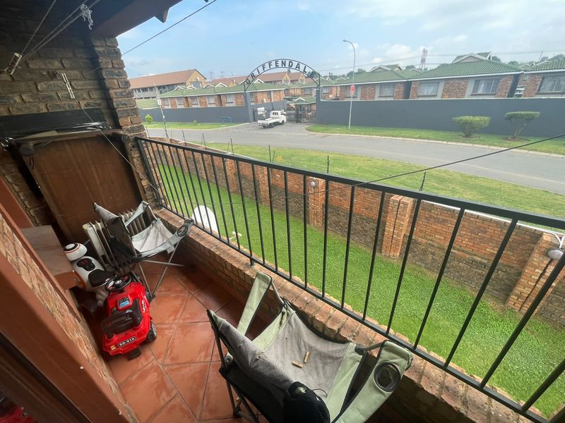 A covered balcony featuring tiled flooring and a metal safety railing, overlooking the complex entrance and street.