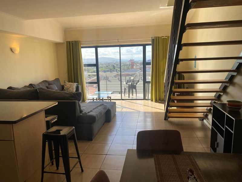 Open-plan living area featuring a modern open-tread staircase, tiled flooring, and large sliding doors leading to a balcony with expansive city views.
