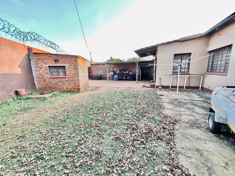 Rear exterior view featuring a brick outbuilding, paved patio area, and security fencing with razor wire.
