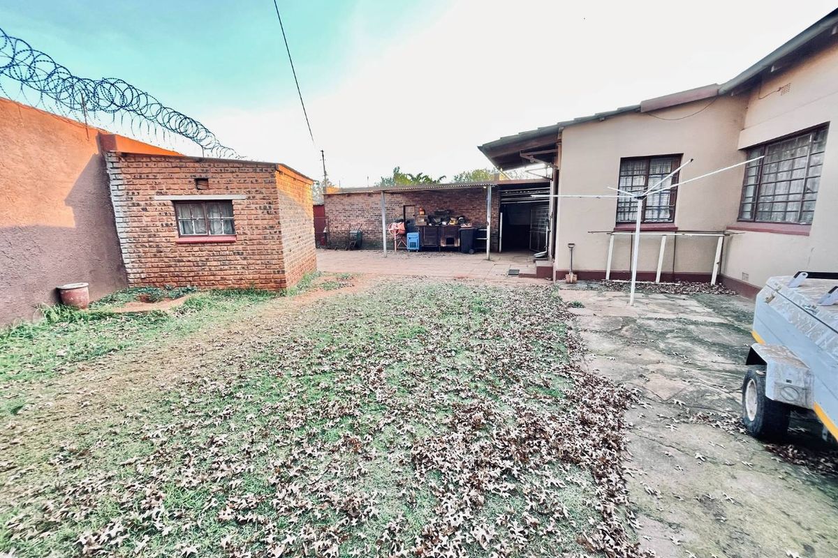 Rear exterior view featuring a brick outbuilding, paved patio area, and security fencing with razor wire.
