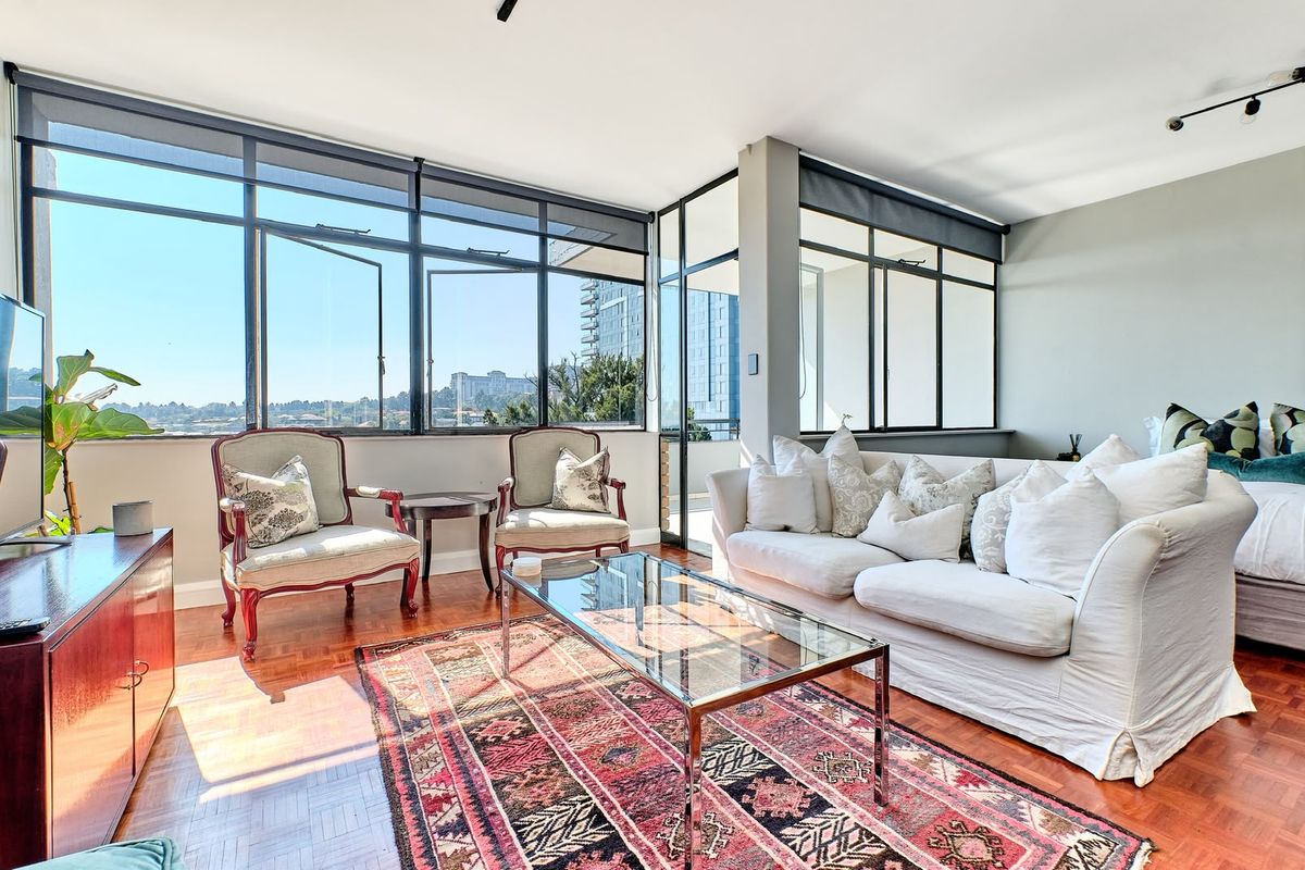 A bright and spacious living area featuring classic parquet flooring and expansive floor-to-ceiling windows that offer abundant natural light and urban views.