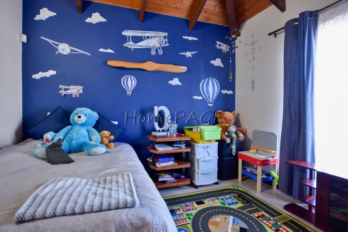 A bedroom featuring exposed timber ceiling beams and a blue feature wall with aviation-themed decor.
