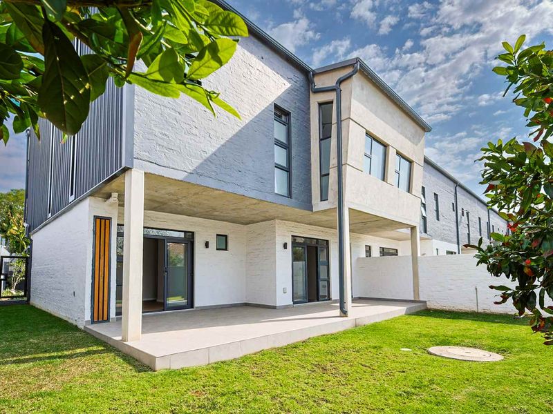Rear view of a modern apartment building featuring a covered patio, tiled flooring, and well-maintained garden space with painted brick exterior finishes.