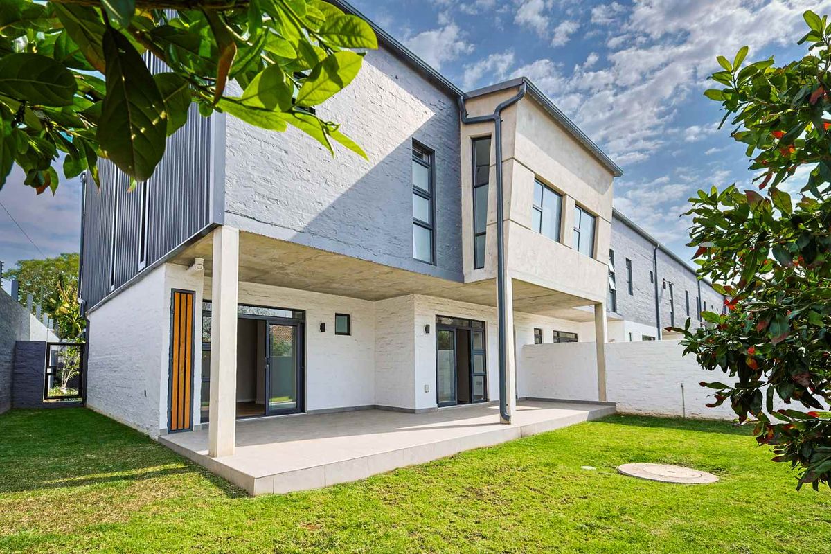 Rear view of a modern apartment building featuring a covered patio, tiled flooring, and well-maintained garden space with painted brick exterior finishes.