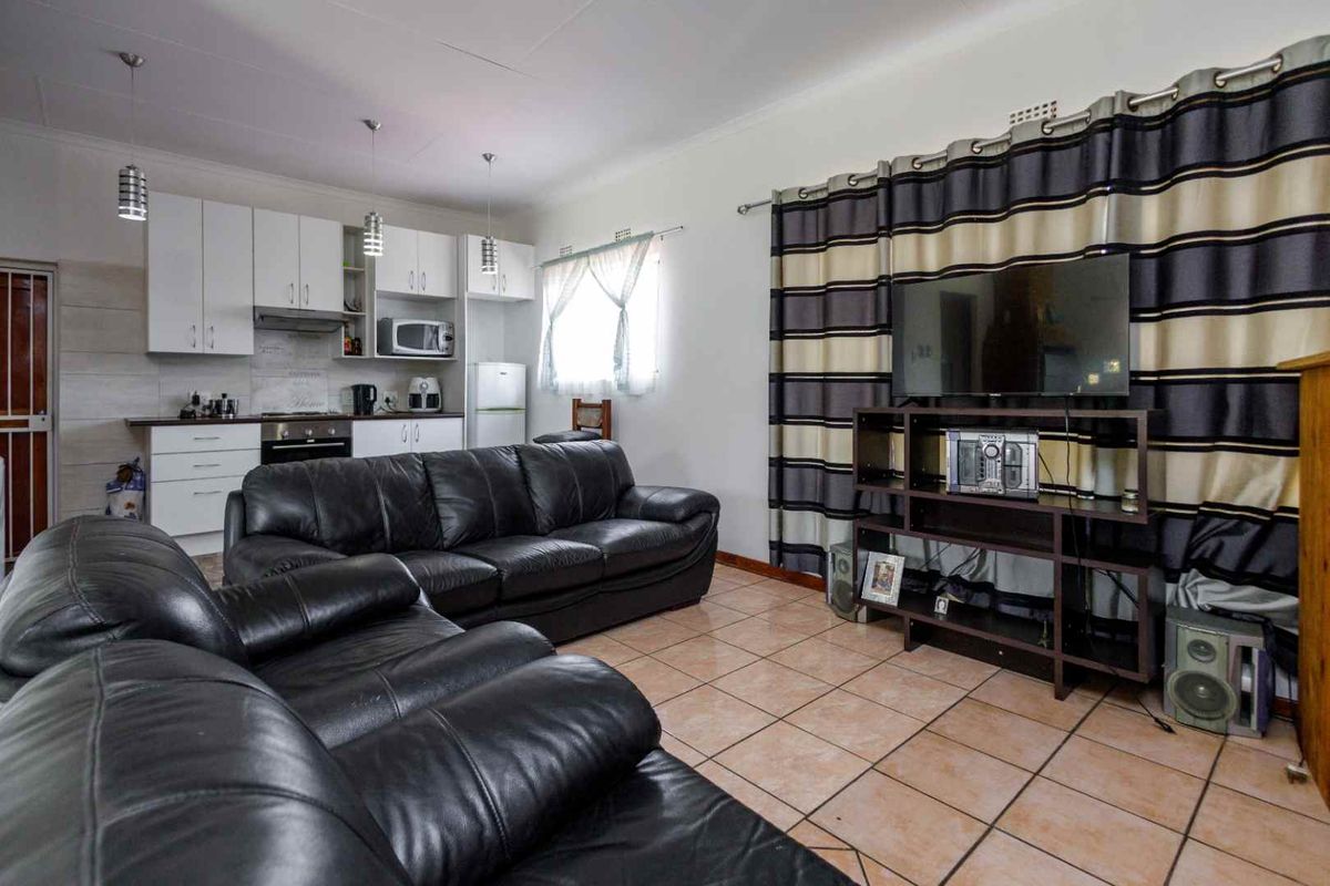Open-plan living area featuring tiled flooring and a compact kitchen with built-in cabinetry, oven, and extractor fan.