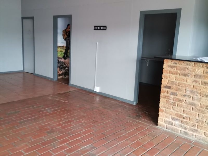 An empty open-plan living area featuring brick accents and tiled flooring, currently in need of finishing touches and cosmetic updates.