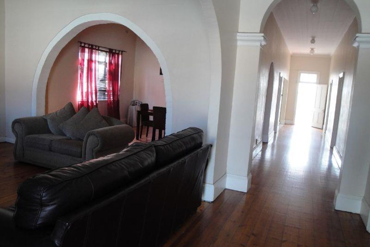 Spacious living area featuring traditional arched doorways, polished hardwood flooring, and a long hallway leading to the entrance.