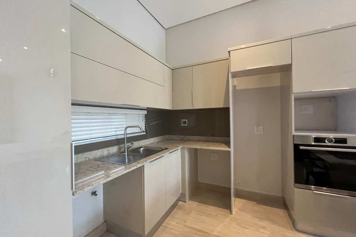Modern kitchen featuring sleek cabinetry, stone-look countertops, stainless steel sink, and a built-in oven, offering a clean and functional culinary space.
