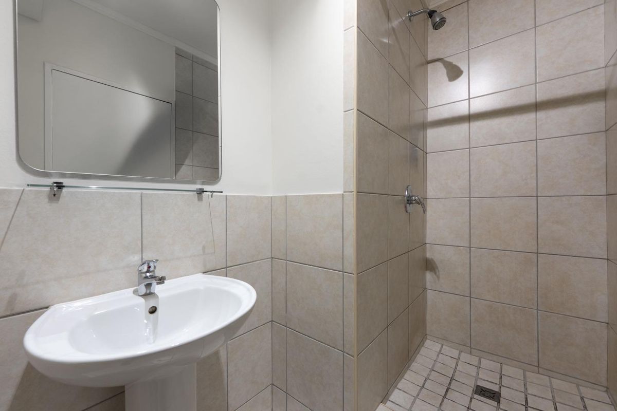 A clean, functional bathroom featuring a pedestal basin, wall-mounted mirror, and a tiled shower enclosure with a fixed shower head.