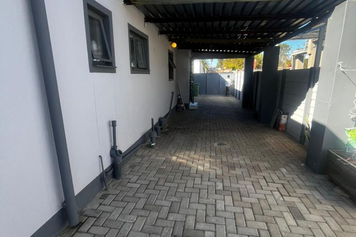 A paved side driveway featuring a covered carport structure and perimeter boundary walls.