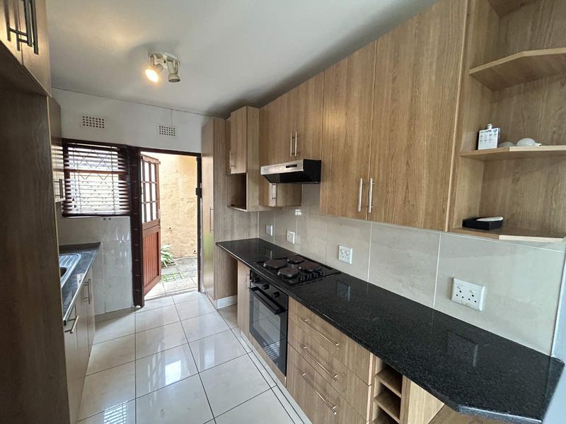 A functional kitchen featuring wood-finish cabinetry, granite countertops, built-in oven and hob, and direct access to an outdoor area.