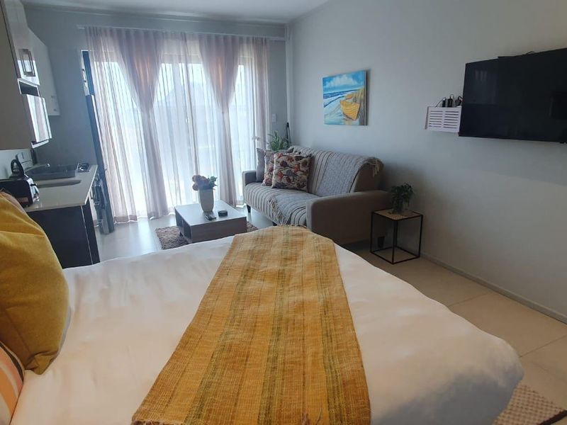 An open-plan studio apartment featuring a compact kitchen area, tiled flooring, and sliding glass doors leading to a balcony.