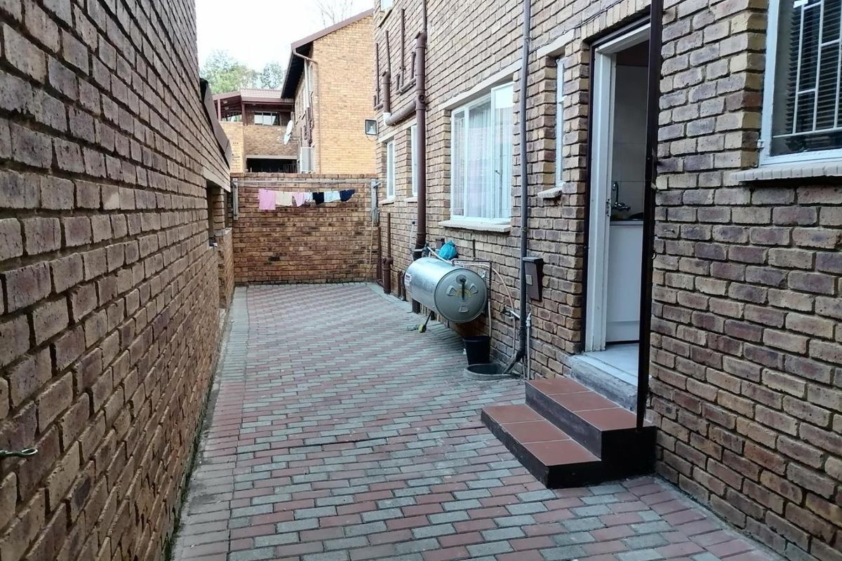 A paved rear courtyard area featuring exposed brick walls, an external geyser unit, and tiled steps leading into the property.