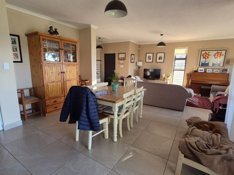 Spacious open-plan living and dining area featuring neutral wall tones, large format floor tiles, and modern pendant lighting throughout the shared space.